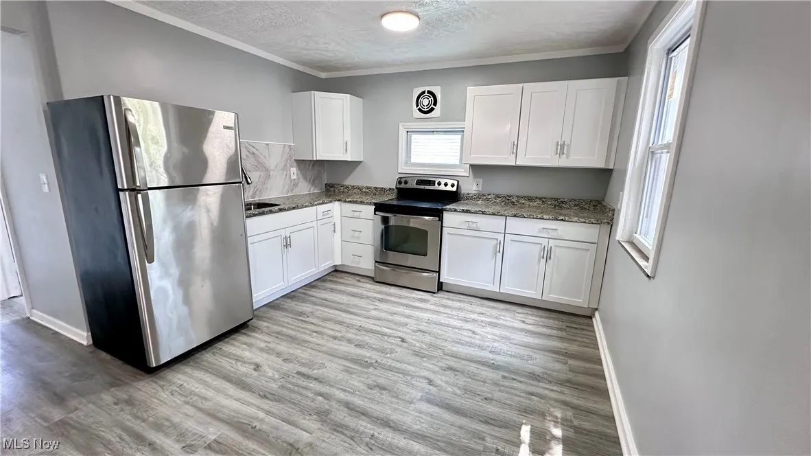 Kitchen featuring appliances with stainless steel finishes, white cabinetry, crown molding, a textured ceiling, and light wood finished floors