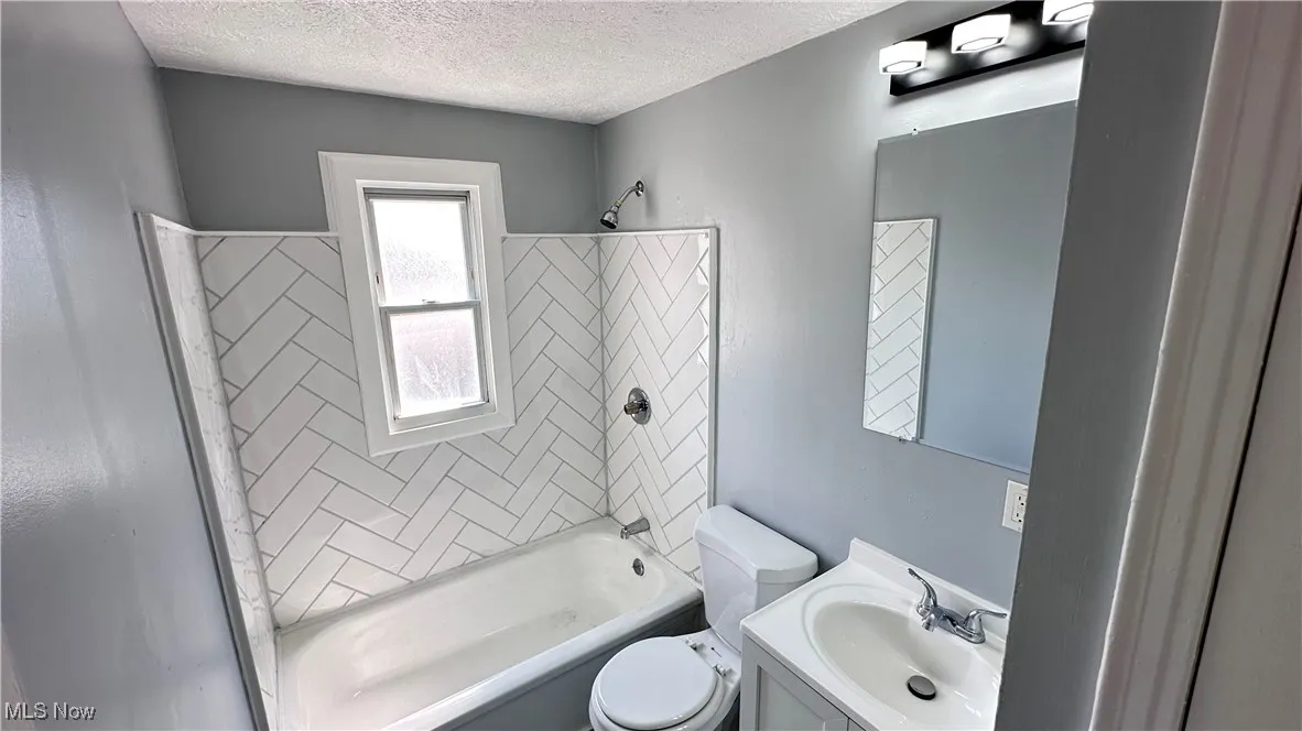 Bathroom featuring tub / shower combination, vanity, and a textured ceiling