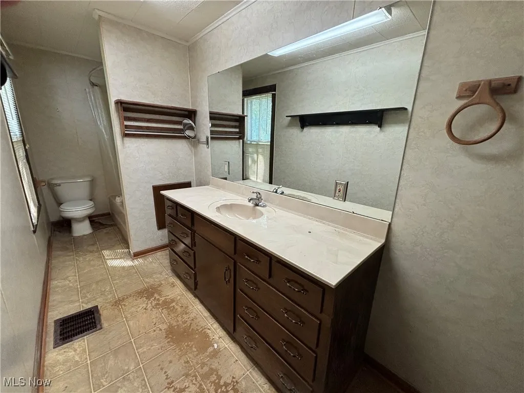 Bathroom with a textured wall, ornamental molding, vanity, and light tile patterned flooring