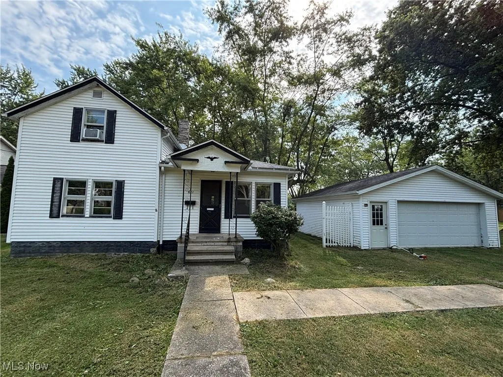 View of front of property featuring a detached garage, a front lawn, and an outbuilding