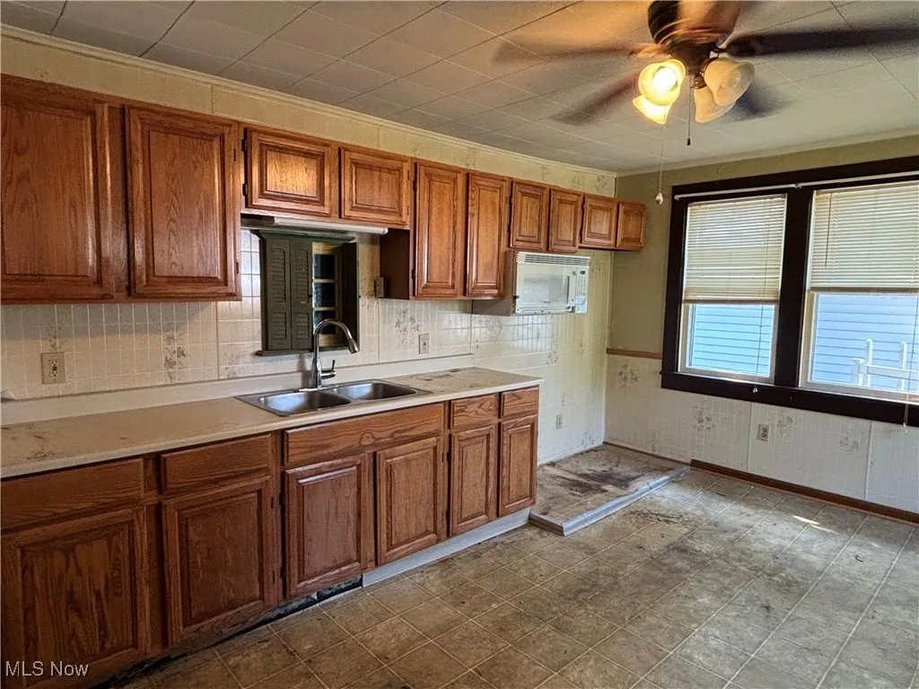 Kitchen with brown cabinetry, light countertops, ceiling fan, backsplash, and white microwave