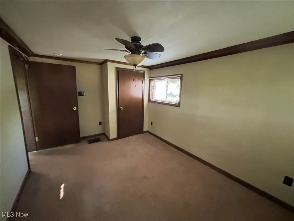 Empty room with crown molding, carpet floors, and ceiling fan