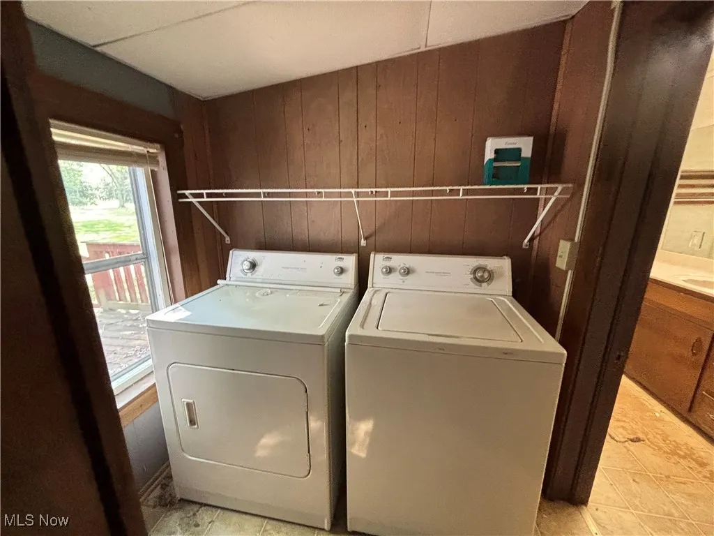 Laundry room with wooden walls, washer and dryer, and light tile patterned floors