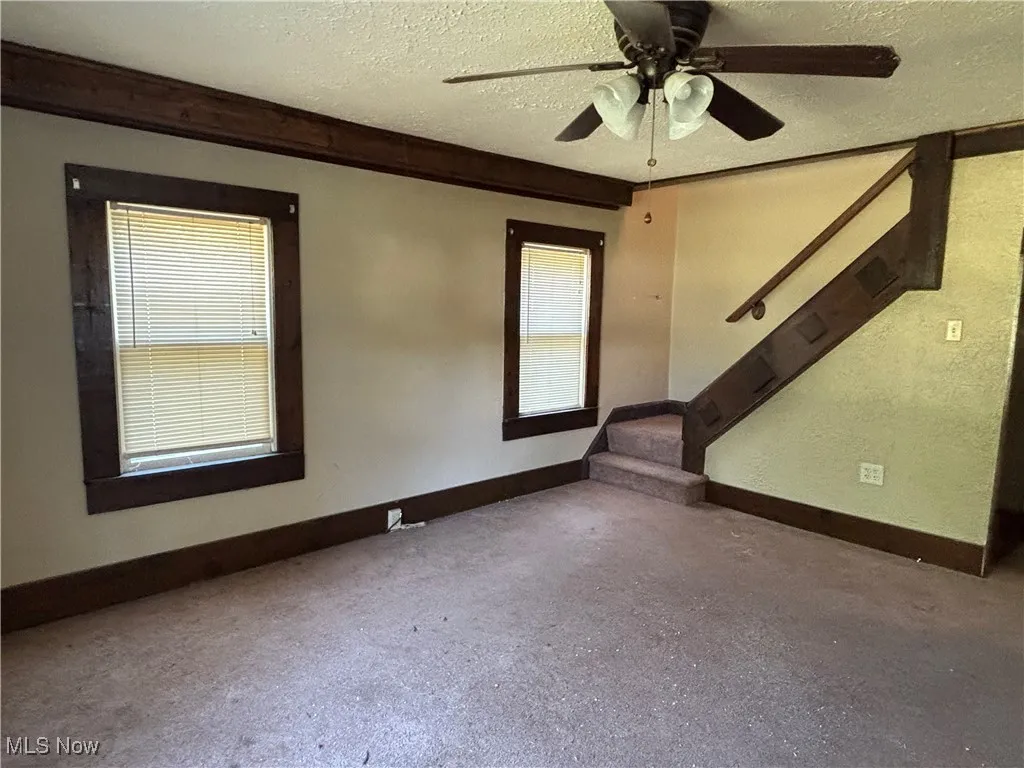 Empty room featuring a textured ceiling, stairs, and a ceiling fan