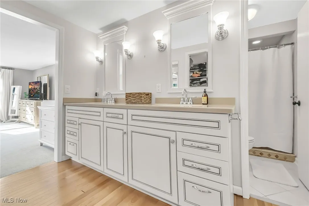 Full bath featuring double vanity, light wood-type flooring, and curtained shower