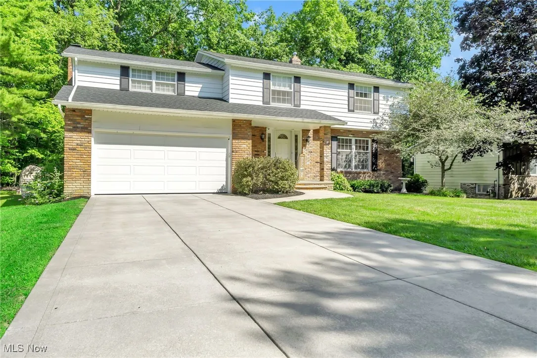 View of front of house with brick siding, driveway, a front lawn, a chimney, and an attached garage