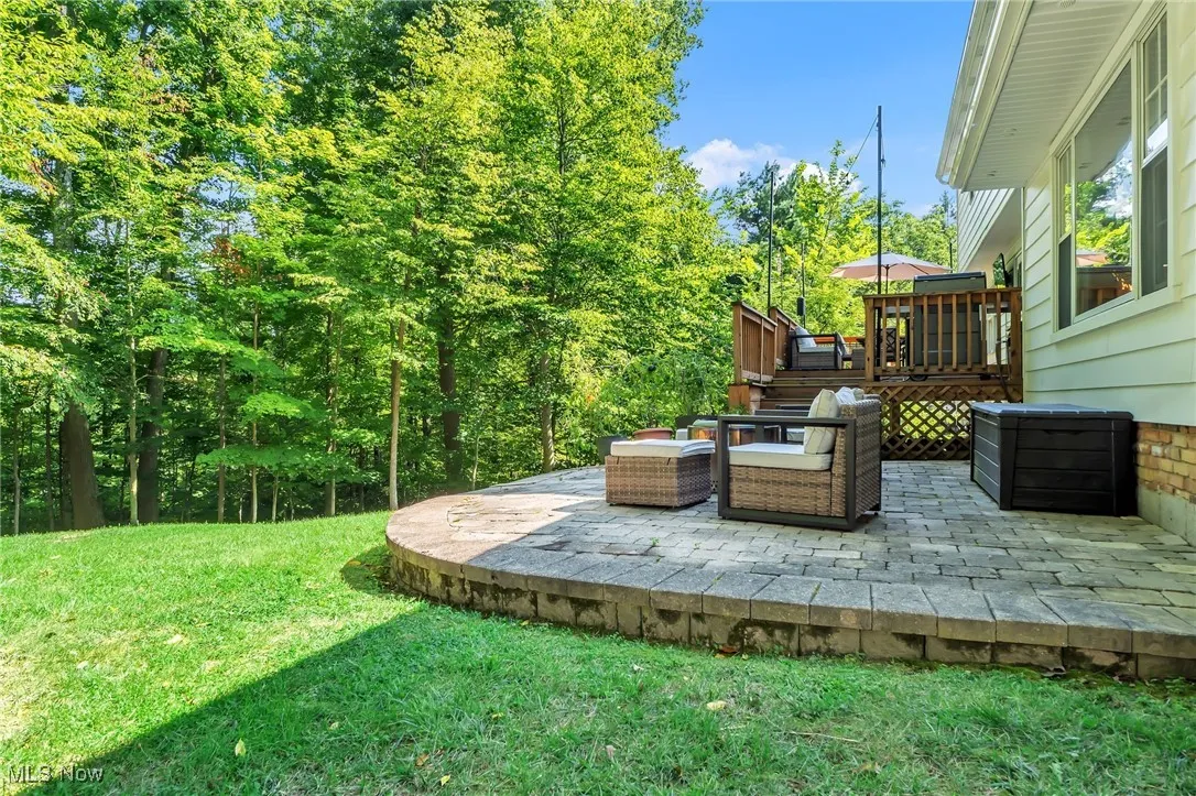 View of green lawn with a patio area, a wooden deck, and view of scattered trees