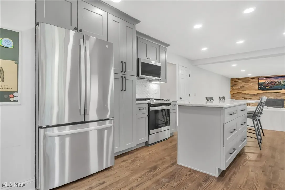 Kitchen with appliances with stainless steel finishes, light wood-type flooring, a kitchen island, recessed lighting, and tasteful backsplash