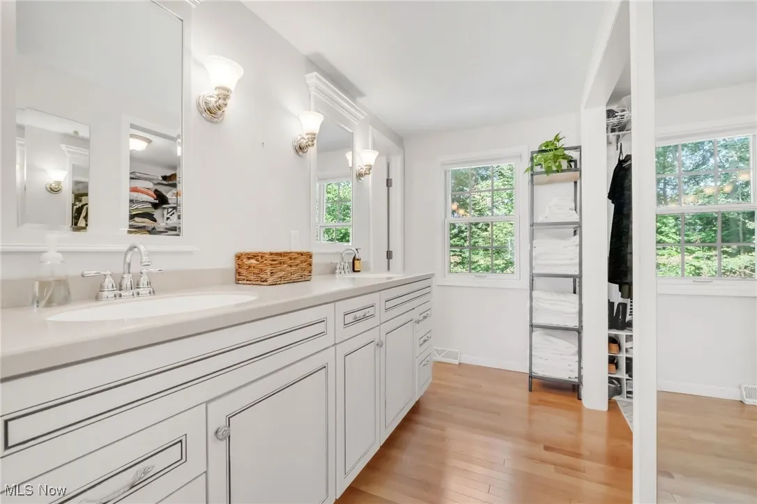 Full bathroom with a spacious closet, double vanity, and light wood-style flooring
