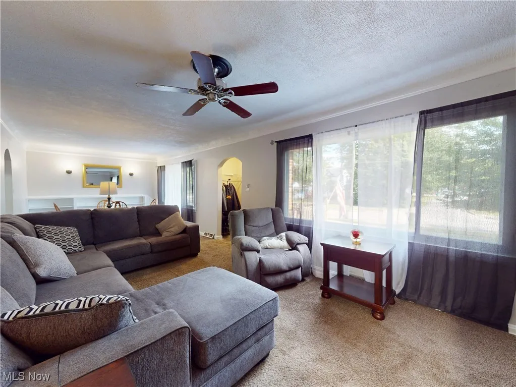 Carpeted living area featuring arched walkways, a textured ceiling, and ceiling fan