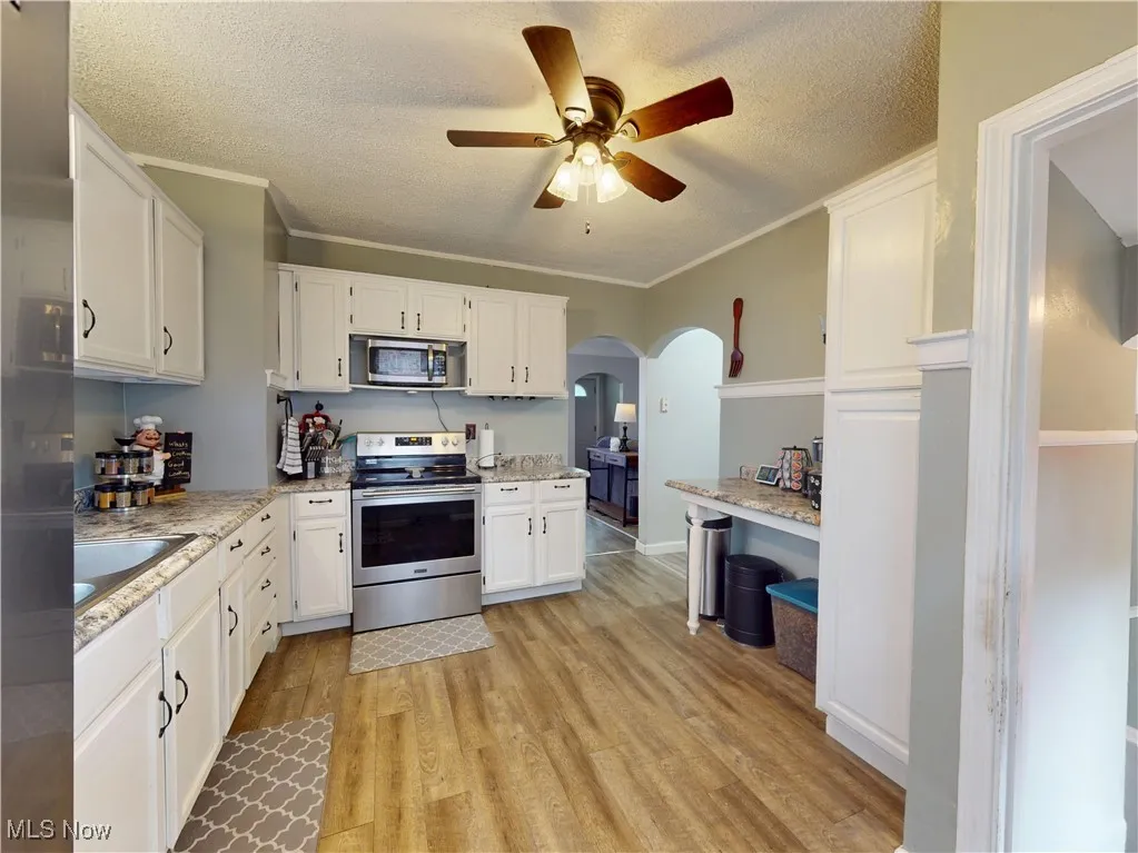 Kitchen featuring stainless steel appliances, a textured ceiling, light wood-style flooring, arched walkways, and white cabinets