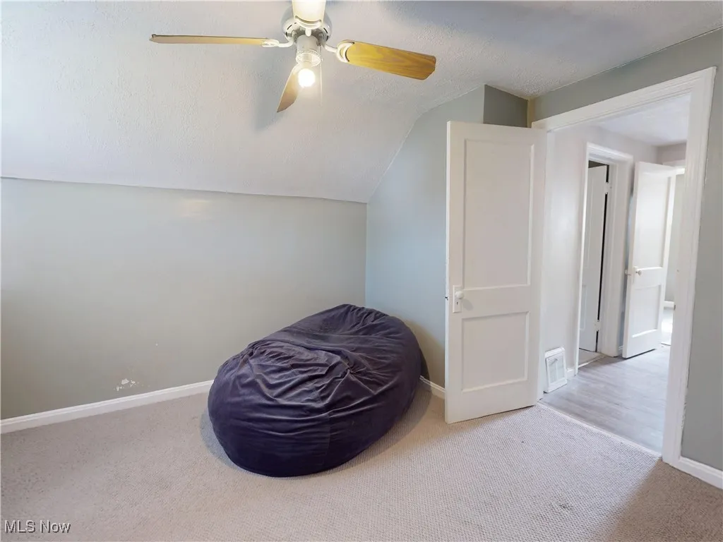 Living area with a textured ceiling, carpet, vaulted ceiling, and ceiling fan