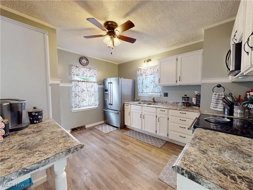 Kitchen featuring white cabinets, a textured ceiling, light wood finished floors, stainless steel appliances, and crown molding