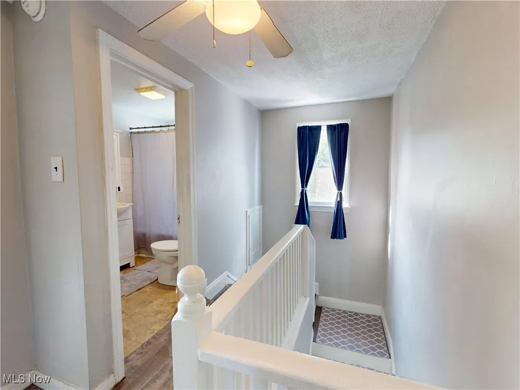 Stairway featuring a textured ceiling, wood finished floors, ceiling fan, and a baseboard radiator
