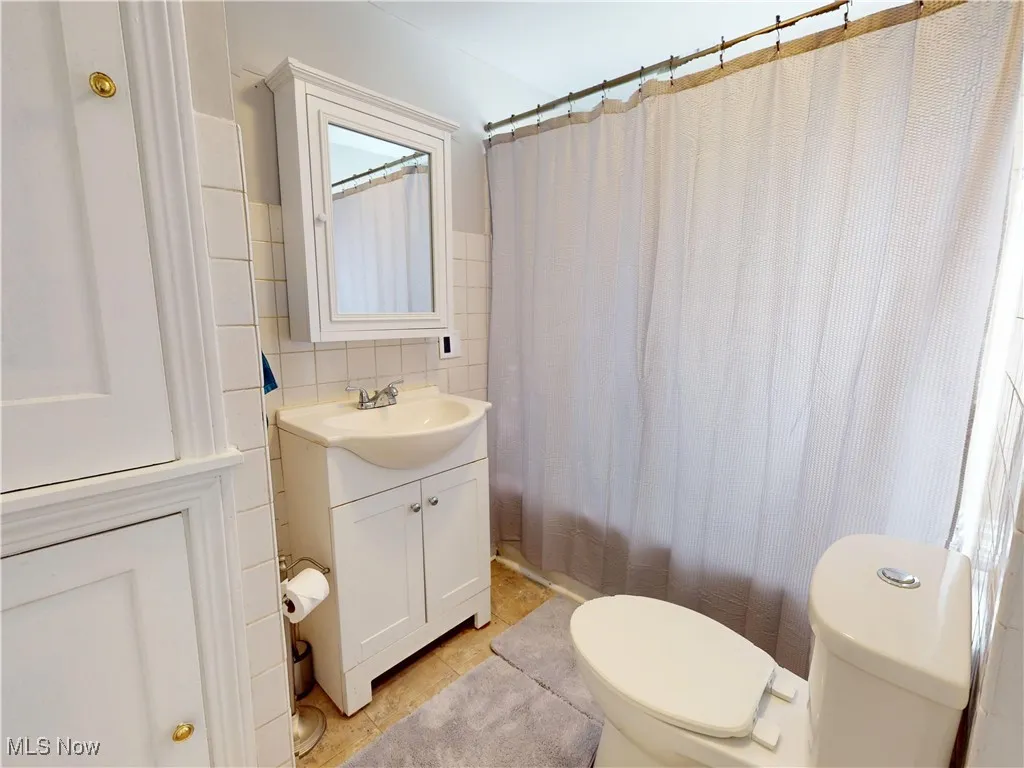 Bathroom featuring vanity, tile walls, shower / bathtub combination with curtain, backsplash, and light tile patterned floors