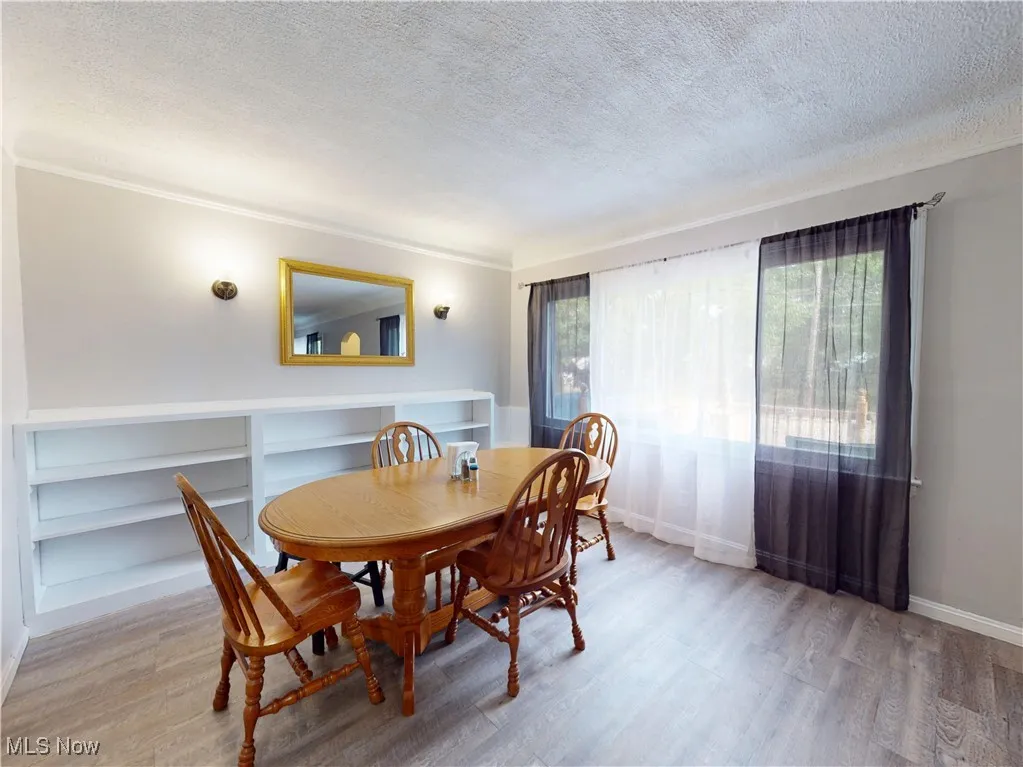 Dining area with a textured ceiling, light wood-style flooring, and ornamental molding