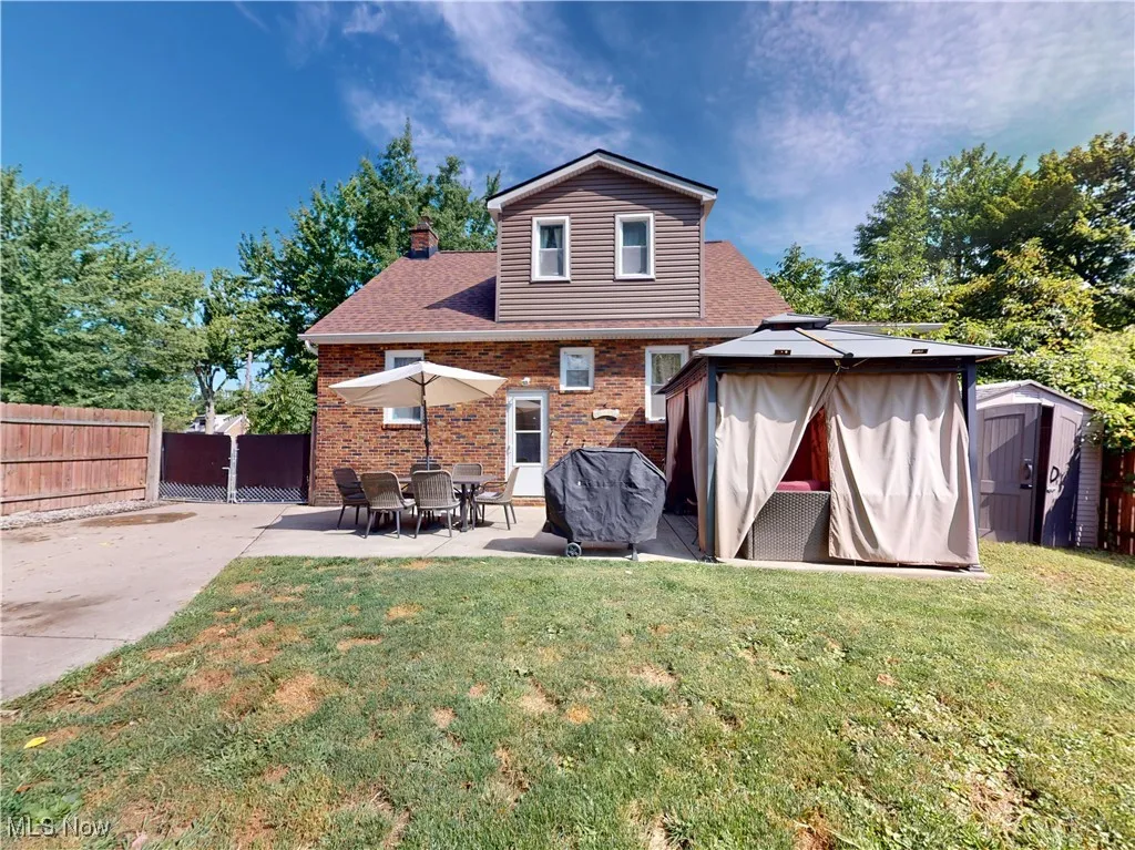 Rear view of property with a shed, a patio area, brick siding, a chimney, and roof with shingles