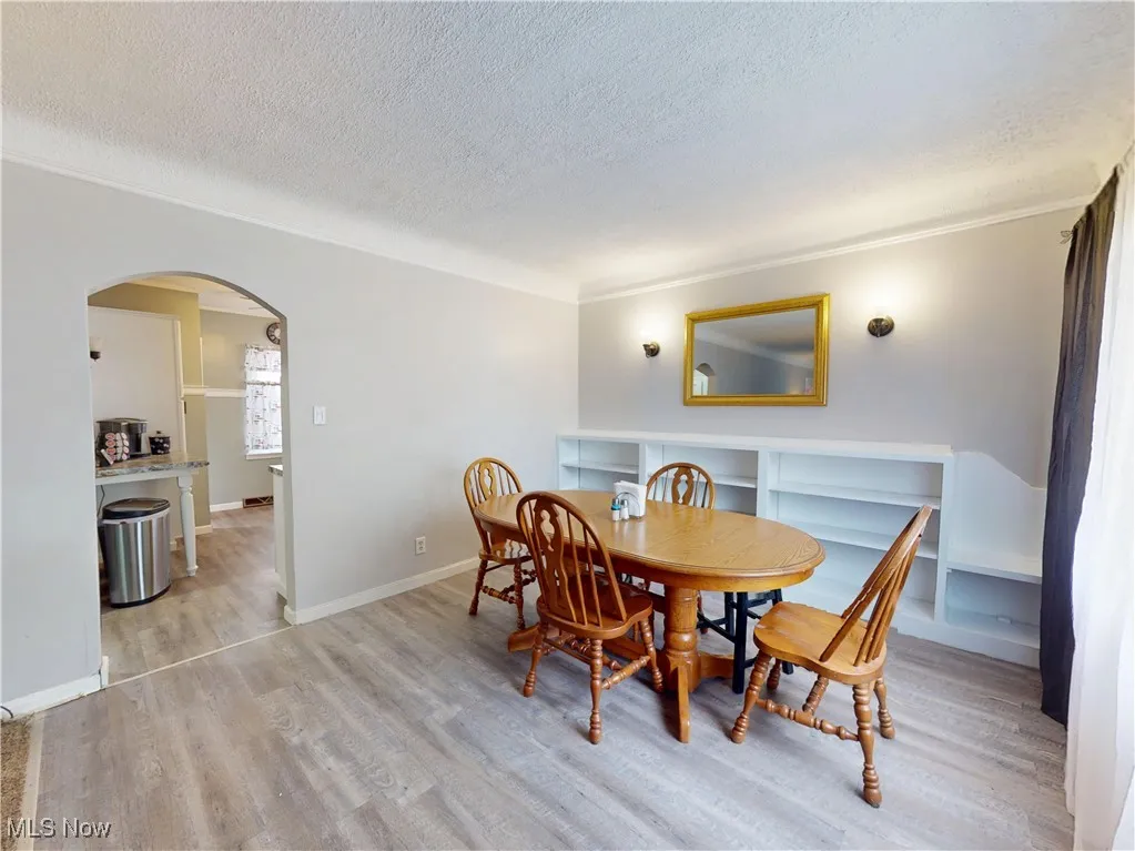 Dining room featuring arched walkways, light wood-style flooring, a textured ceiling, and ornamental molding
