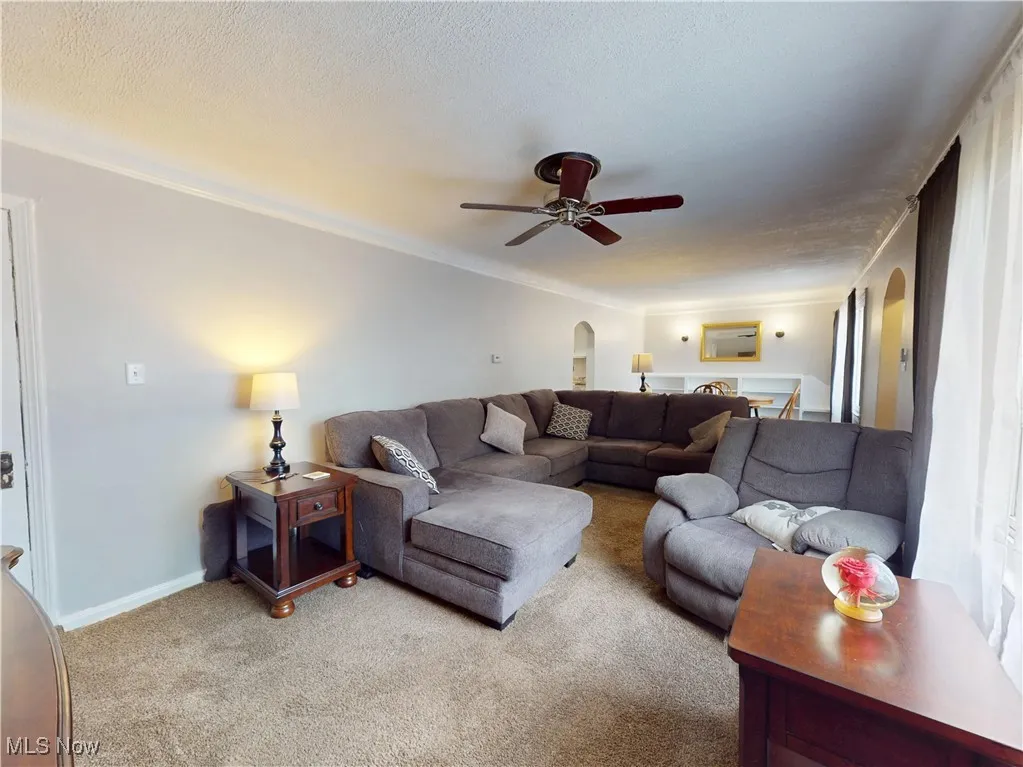 Living room featuring arched walkways, carpet floors, a ceiling fan, and a textured ceiling