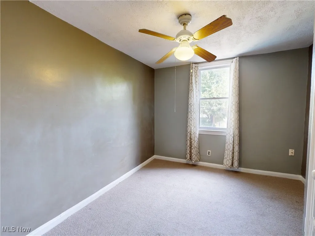 Empty room with carpet, a textured ceiling, and ceiling fan