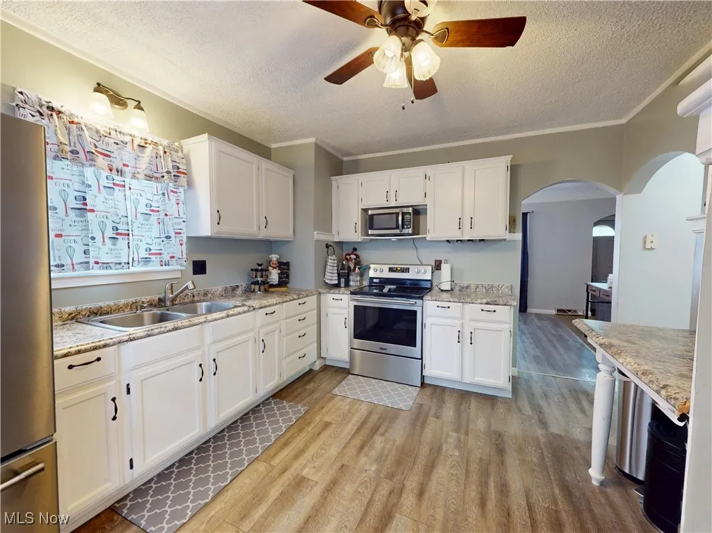 Kitchen featuring appliances with stainless steel finishes, white cabinets, light wood-style floors, a textured ceiling, and a ceiling fan