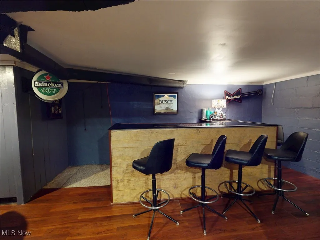 Indoor dry bar with dark wood finished floors, concrete block wall, and dark countertops