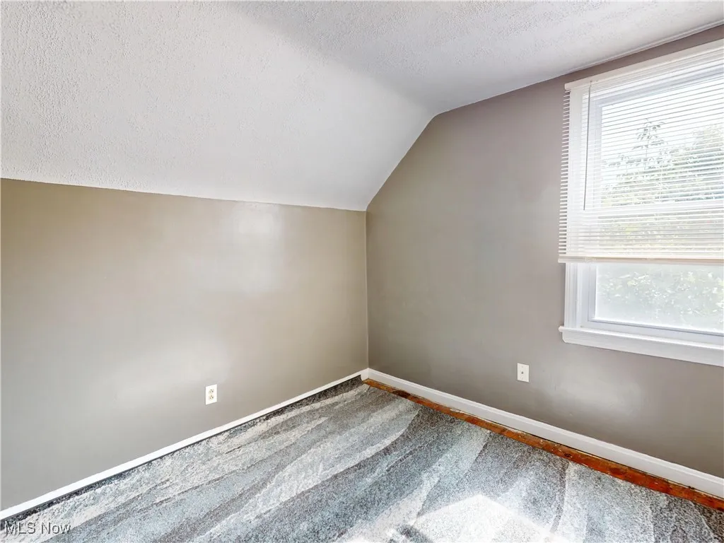 Additional living space with a textured ceiling, healthy amount of natural light, vaulted ceiling, and wood finished floors