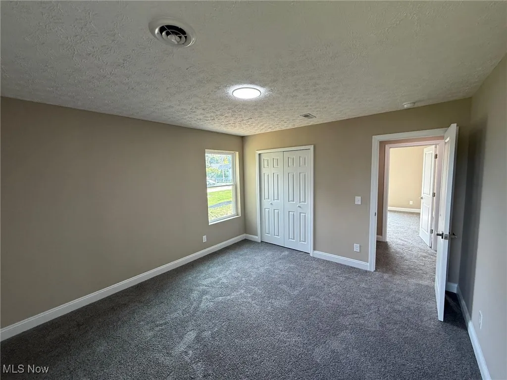 Unfurnished bedroom with dark colored carpet, a textured ceiling, and a closet