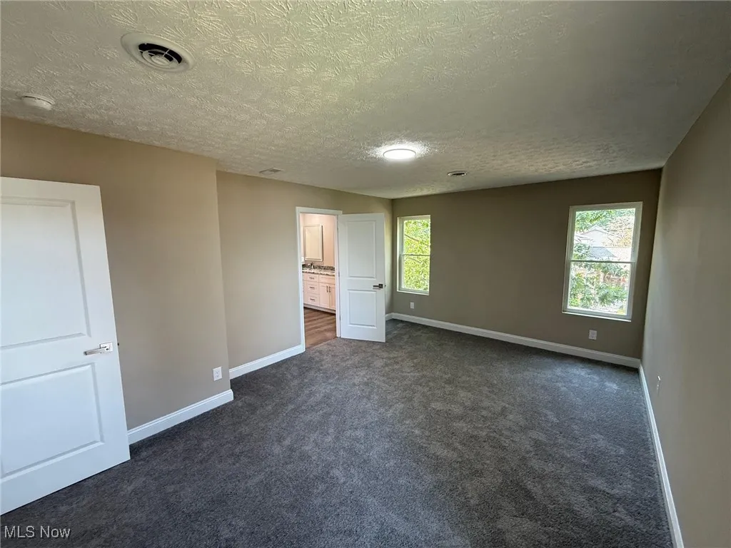 Unfurnished bedroom featuring dark colored carpet, a textured ceiling, and ensuite bath