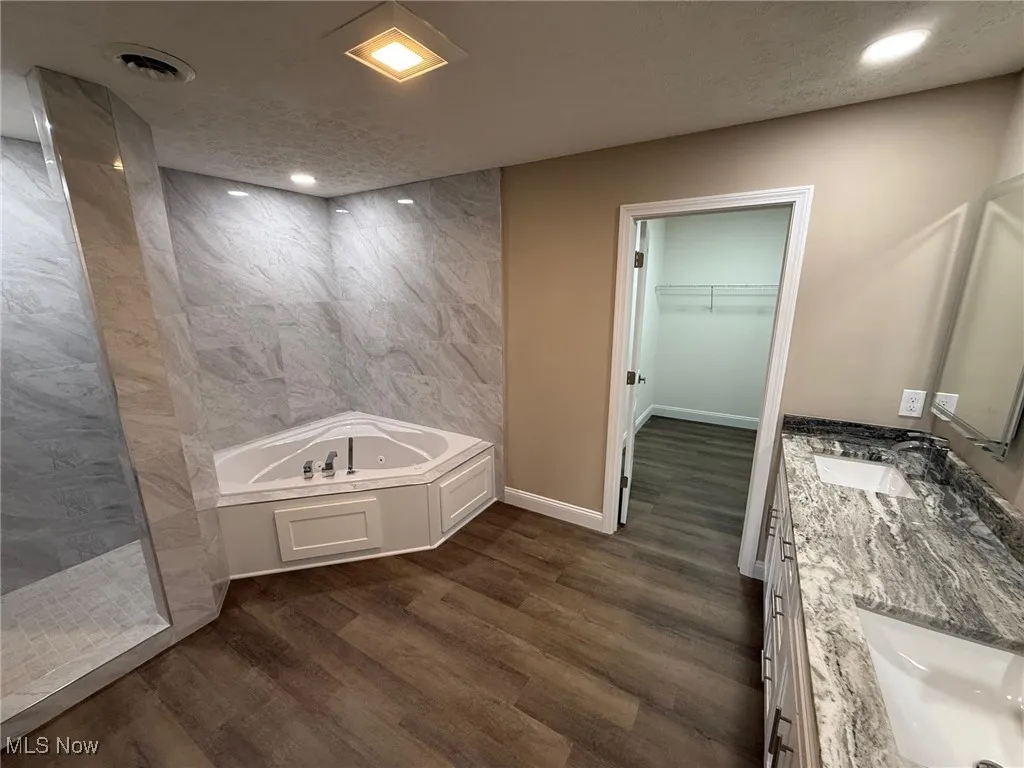 Full bathroom with a walk in closet, walk in shower, double vanity, a bath, and dark wood-style flooring