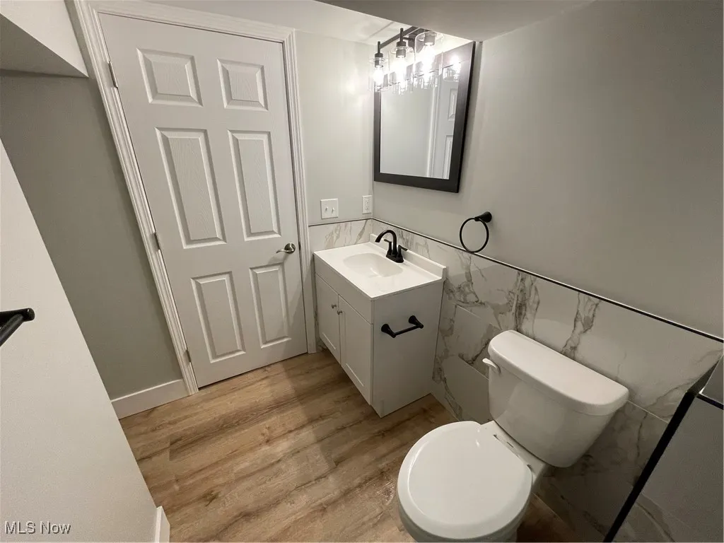 Full bathroom with tile walls, vanity, light wood-style flooring, and wainscoting