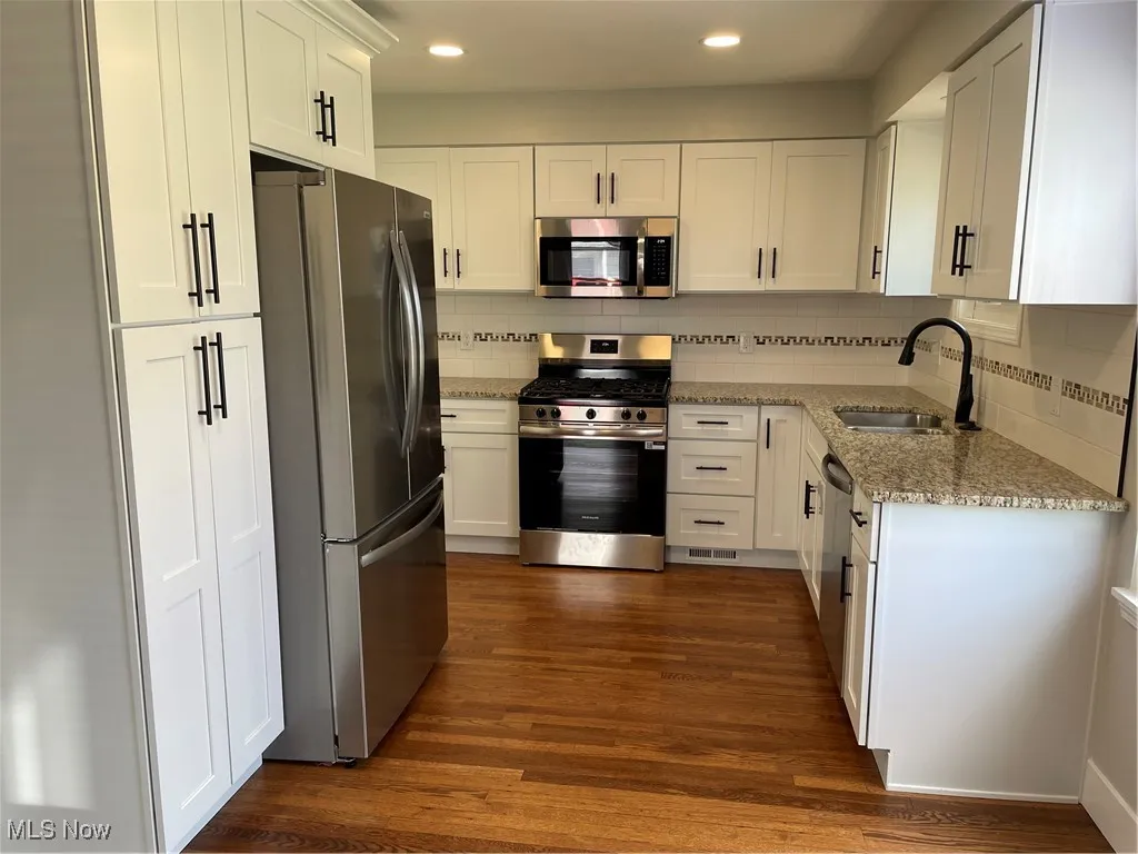 Kitchen with light stone counters, stainless steel appliances, decorative backsplash, white cabinets, and recessed lighting