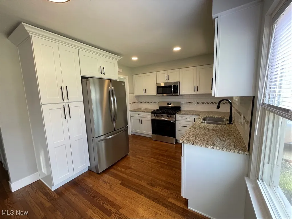 Kitchen featuring light stone counters, white cabinets, appliances with stainless steel finishes, dark wood finished floors, and decorative backsplash