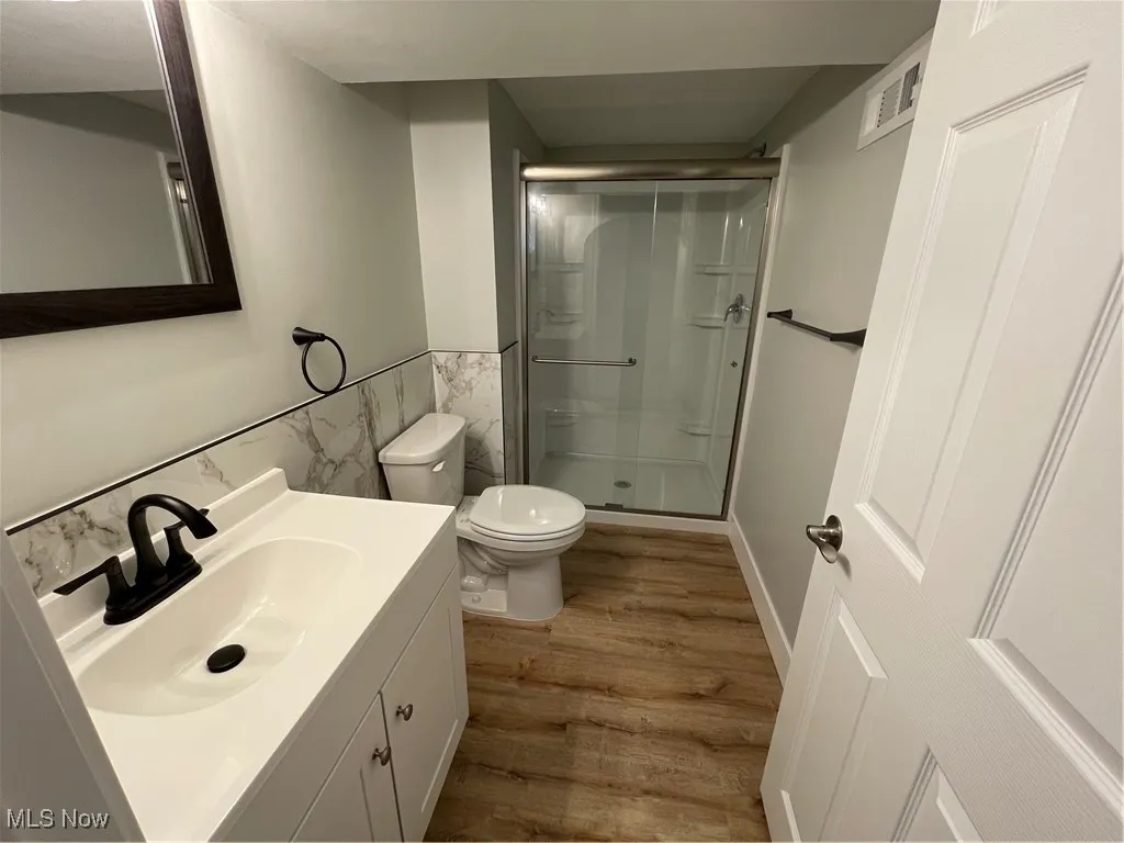Full bath featuring vanity, wood finished floors, a stall shower, tile walls, and wainscoting