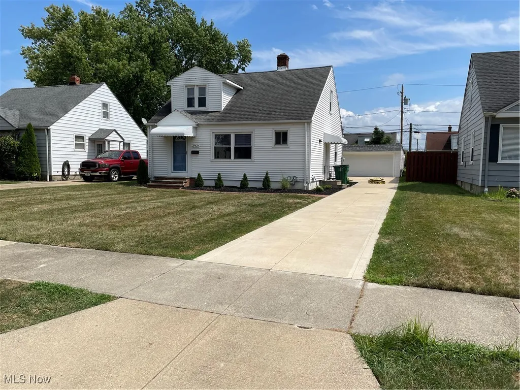 View of front of house with an outbuilding, roof with shingles, a chimney, a front lawn, and a detached garage