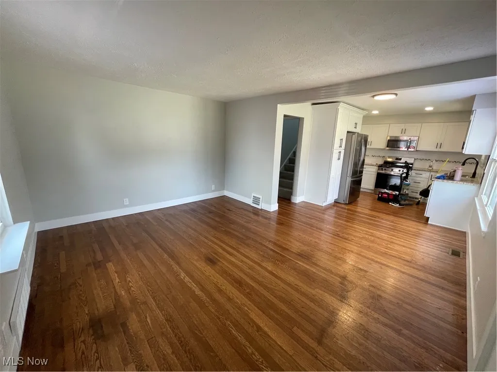 Unfurnished living room featuring dark wood-style floors, a textured ceiling, stairway, and recessed lighting
