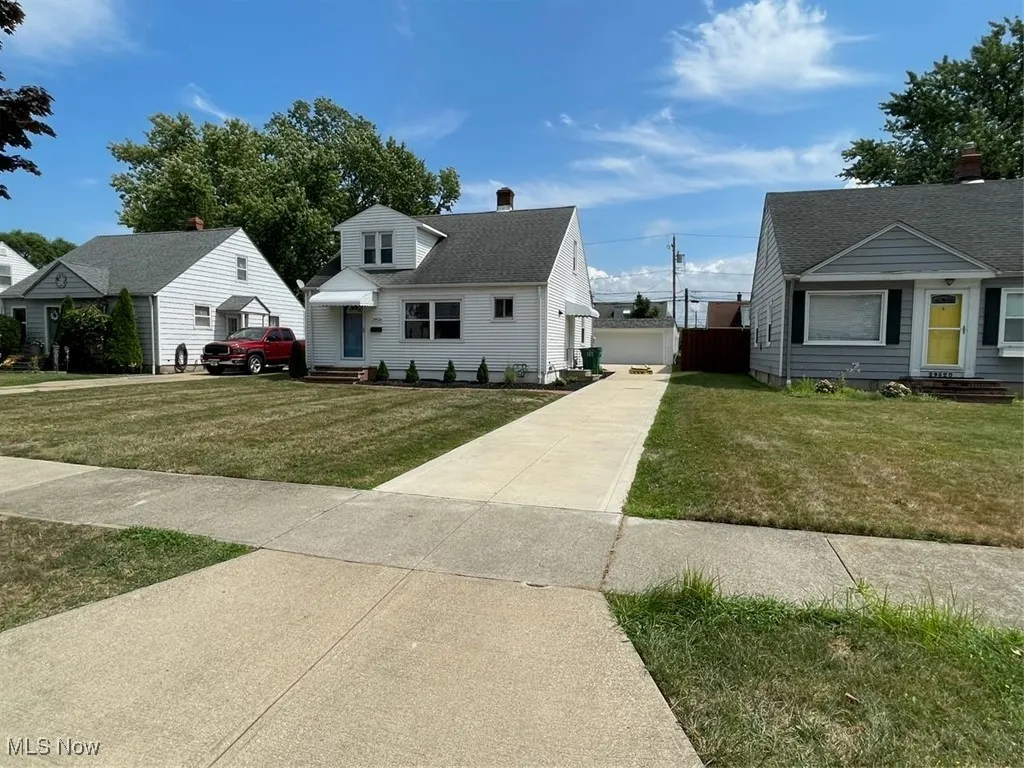 View of front of house featuring a front lawn, a shingled roof, a chimney, and a garage
