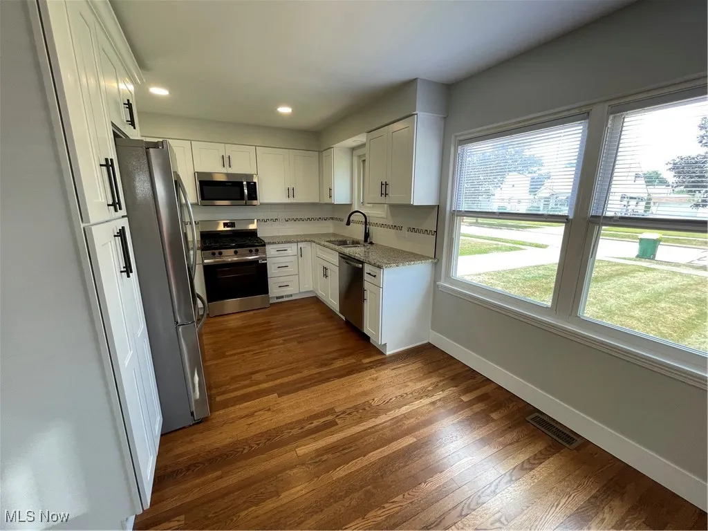 Kitchen featuring white cabinets, stove, white refrigerator, light stone counters, and dark wood-style flooring