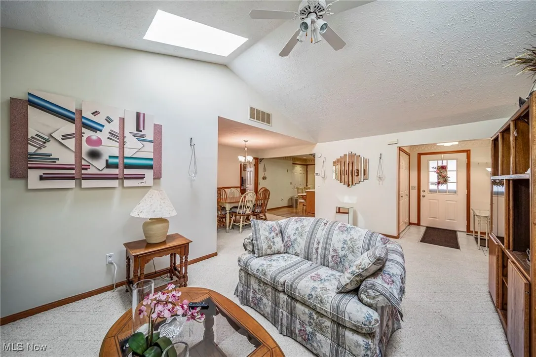 Living area with a textured ceiling, light carpet, a skylight, ceiling fan, and a chandelier
