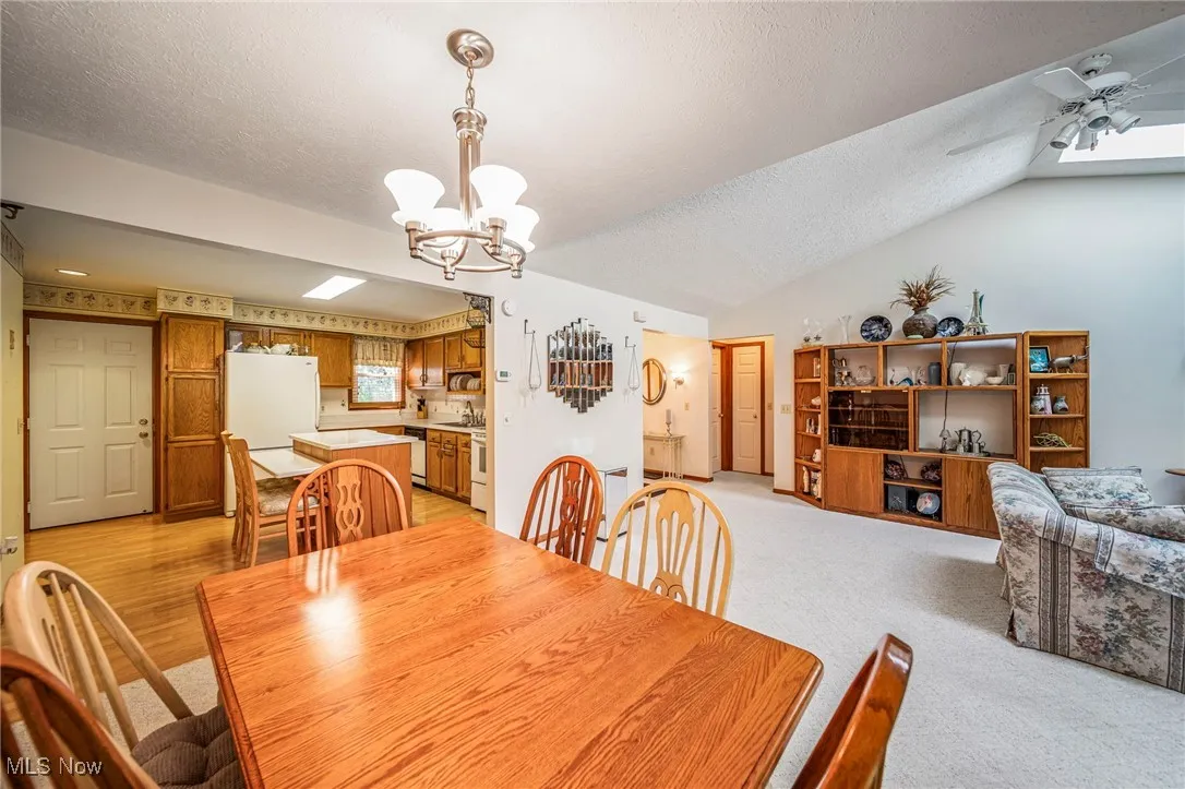 Dining room with a textured ceiling, a ceiling fan, light carpet, a chandelier, and lofted ceiling