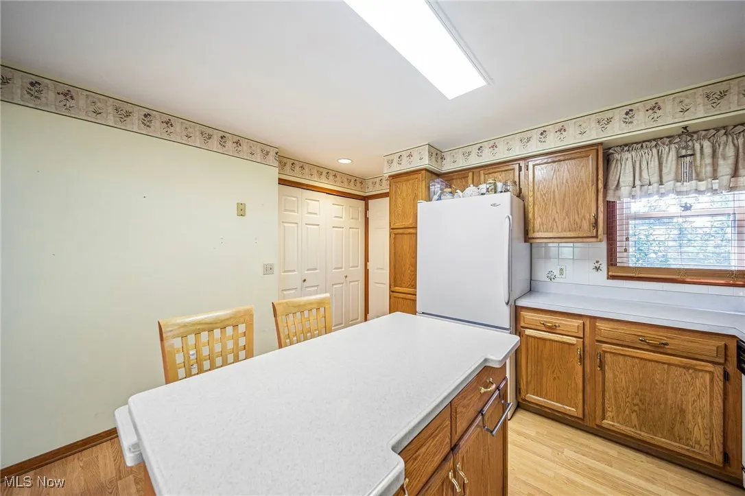 Kitchen featuring light countertops, freestanding refrigerator, light wood-style floors, and brown cabinets