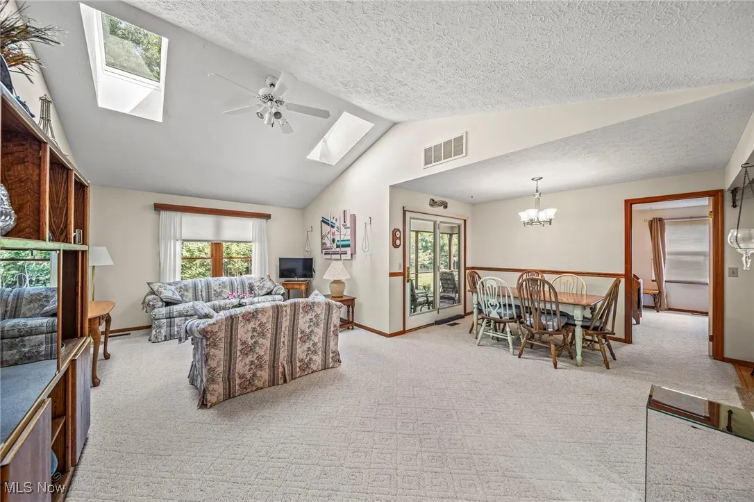 Living room featuring carpet, a skylight, a ceiling fan, a textured ceiling, and high vaulted ceiling