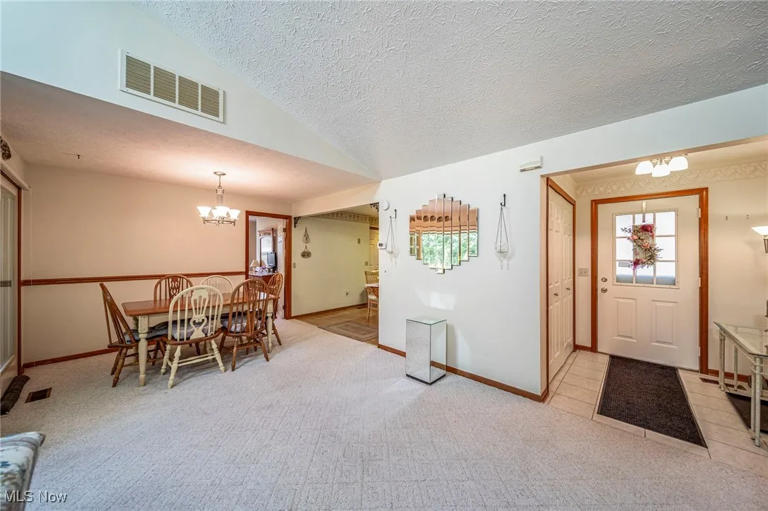 Dining room with a chandelier, a textured ceiling, plenty of natural light, lofted ceiling, and light carpet