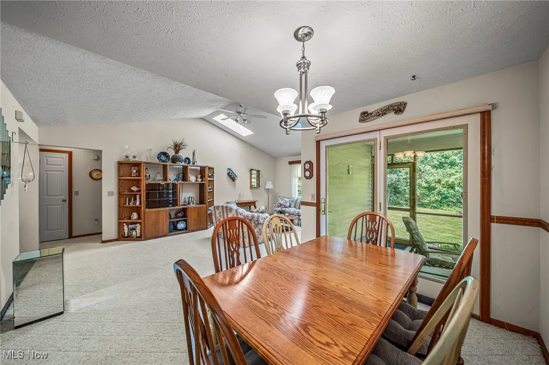 Dining area featuring carpet, a textured ceiling, a chandelier, lofted ceiling, and ceiling fan