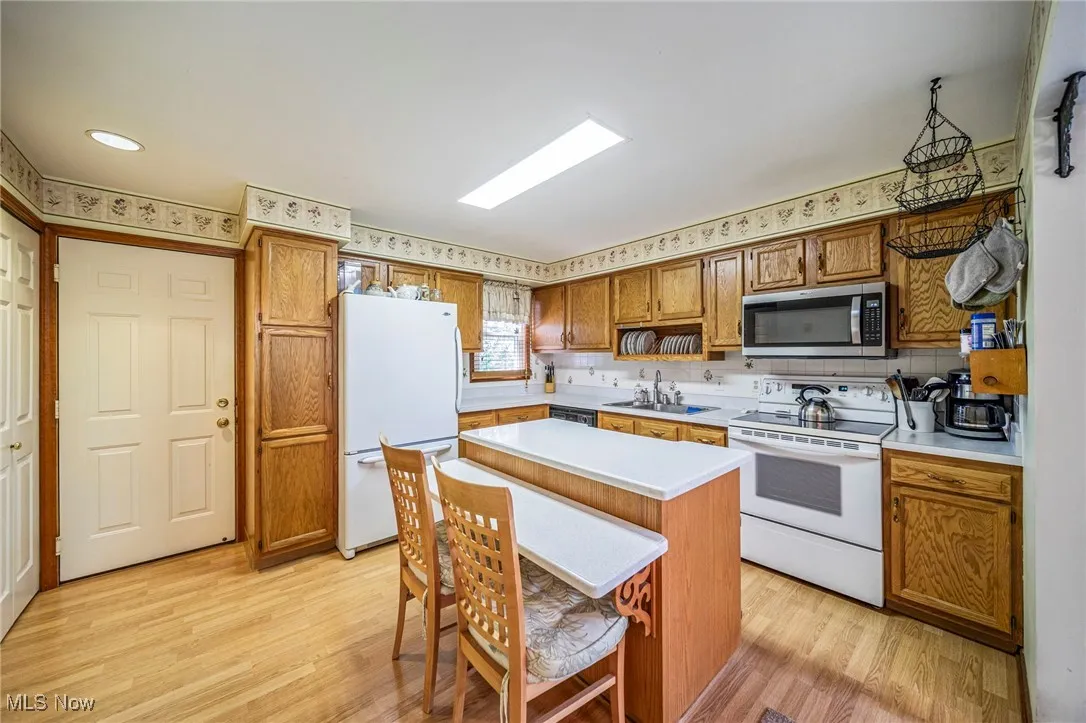 Kitchen featuring white appliances, light countertops, brown cabinets, and light wood-style flooring