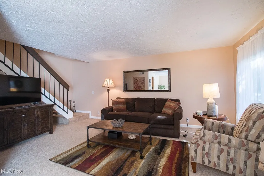 Carpeted living room featuring a textured ceiling and​​‌​​​​‌​​‌‌​‌‌​​​‌‌​‌​‌​‌​​​‌​​ stairway