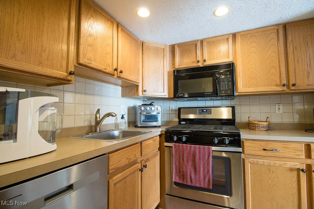 Kitchen featuring appliances with stainless steel finishes, light countertops, a textured ceiling, backsplash, and recessed lighting