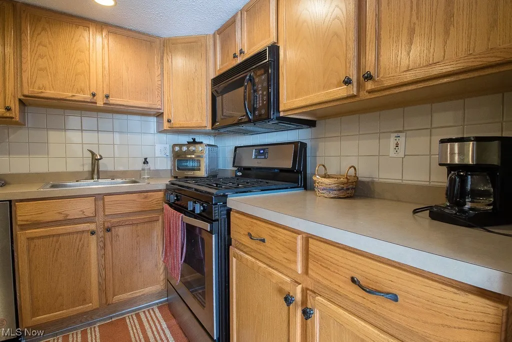 Kitchen with stainless steel gas stove, tasteful backsplash, light countertops, a textured ceiling, and black microwave
