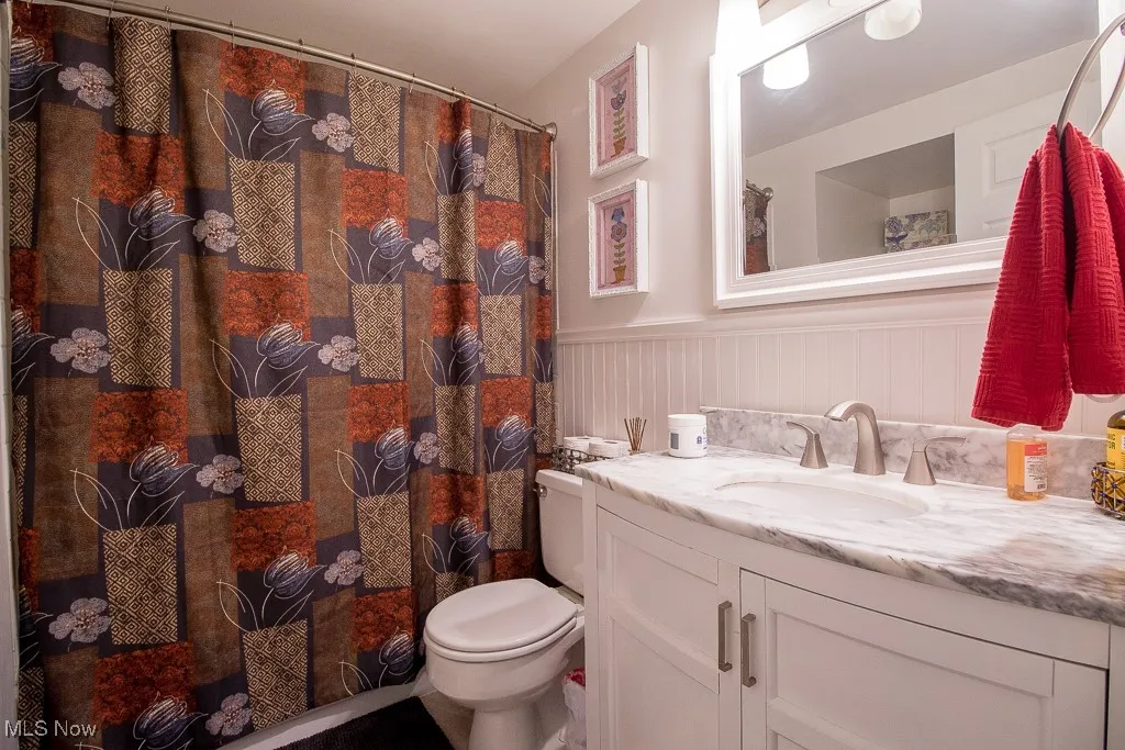 Full bathroom featuring vanity, a wainscoted wall, and a stall shower