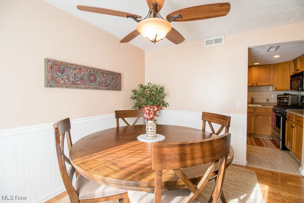 Dining area featuring a wainscoted wall, a textured ceiling, ceiling fan, and light wood finished floors